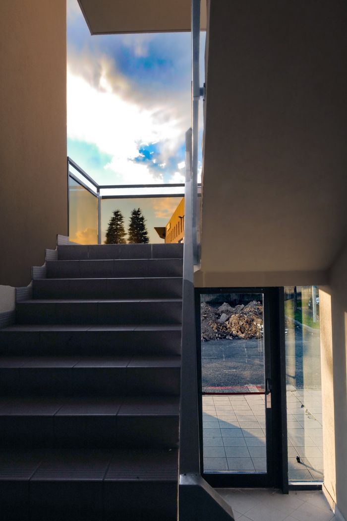Minimalist staircase with glass railings offering a view of the sky and outdoors, capturing sunset tones.